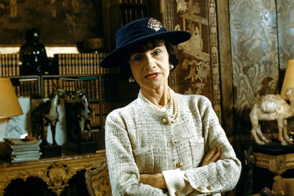 Коко Шанель у класичному твідовому жакеті та капелюсі у власному інтер’єрі