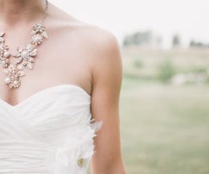 Close-up of a floral necklace adorning a bride in a strapless white wedding dress outdoors.
